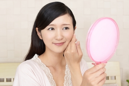 鏡を見て頬を触る女性